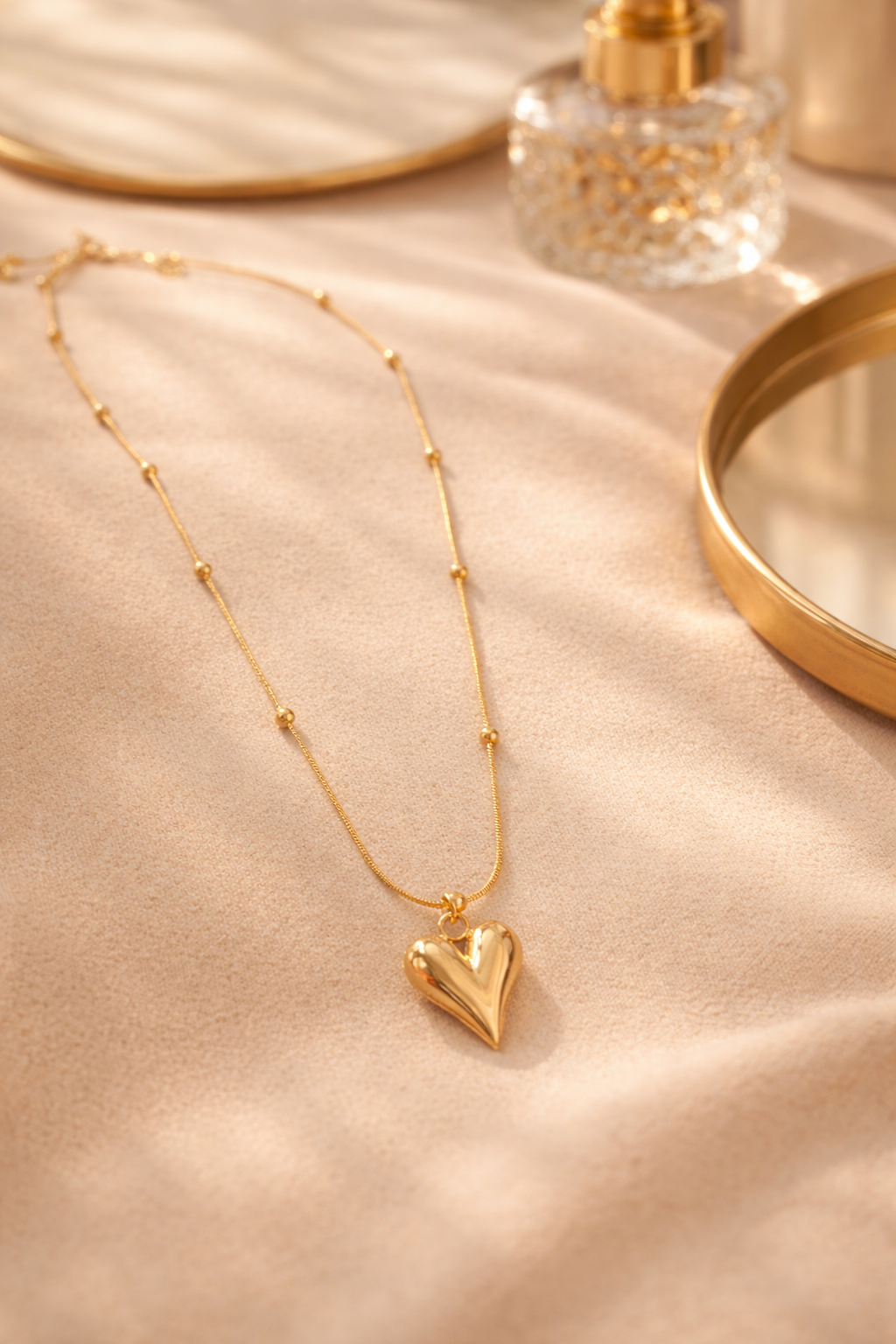 Gold heart-shaped necklace on a beige fabric background with a perfume bottle.